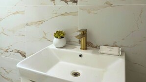 Ein weißes Waschbecken mit goldener Armatur, ein kleiner Topfpflanze und ein Schild mit dem Hotelnamen.