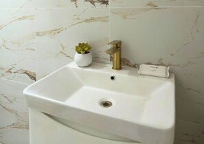 Ein weißes Waschbecken mit goldener Armatur, ein kleiner Topfpflanze und ein Schild mit dem Hotelnamen.