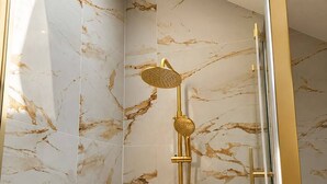 Eine moderne Dusche mit goldfarbener Duschbrause und Handbrause, vor Marmorwänden.