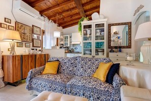 Una sala acogedora con un sofá floral, un aparador de madera y una cocina al fondo.