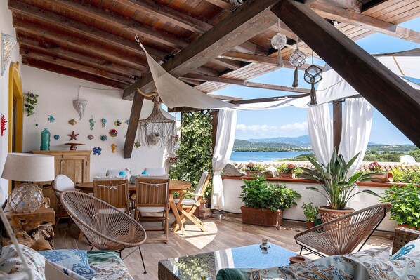 Un rincón al aire libre acogedor con sillas de mimbre, una mesa y plantas en macetas.