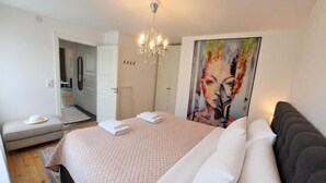 Ein Schlafzimmer mit einem Bett, einem Gemälde, einer Chandelieber und einer Tür zu einem weiteren Raum.