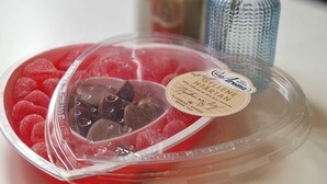 Ein Dessertteller mit einer herzförmigen Abdeckung, gefüllt mit roter und dunkler Schokolade, und ein kleines blaues Glasgefäß mit einer Pflanze im Hintergrund.