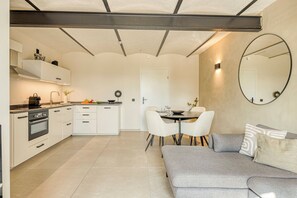 A modern kitchen with white cabinetry, a dining area with a round table and chairs, and a grey sofa with cushions.