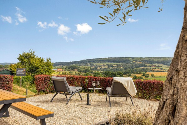 An outdoor seating area with two chairs and a table, a sign, and a view of rolling hills.