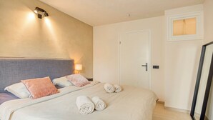 Ett hotellrum med en säng, kuddar, en sänglampa, en dörr och en spegel.