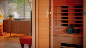 Un intérieur en bois avec un banc, une fenêtre avec des stores et une petite étagère sur laquelle sont posés divers objets.