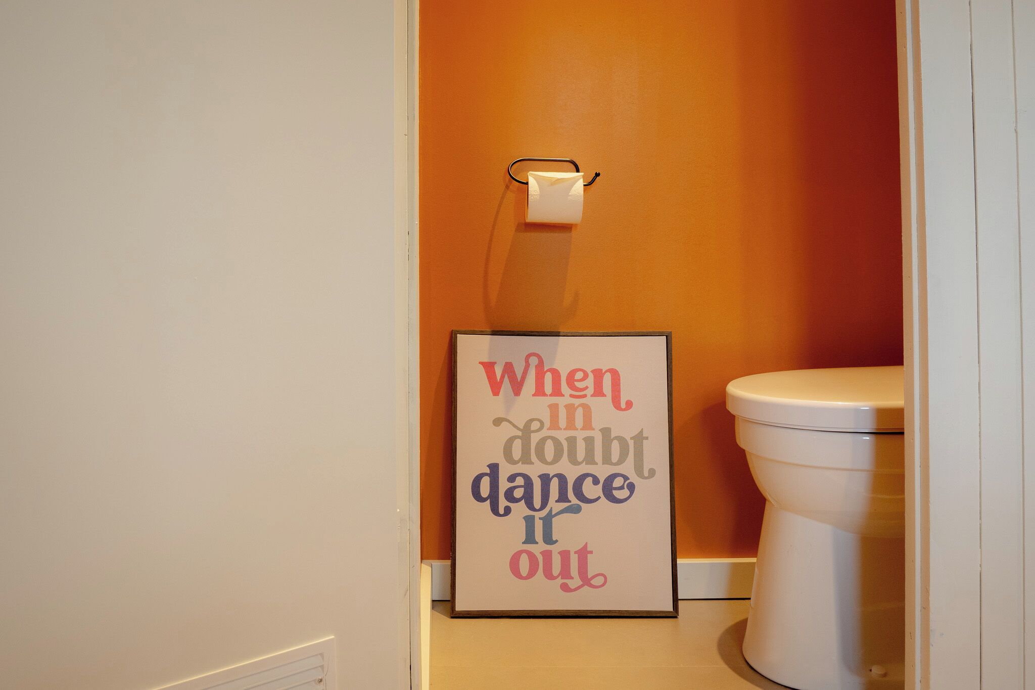 A bathroom with a toilet, a roll of toilet paper, and a motivational quote poster.