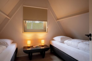 Una habitación pequeña y triangular con dos camas, una ventana y una mesita de noche con lámparas.