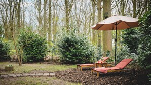 Een tuin met een houten bankje, een tafel met een rood kussen en een grote parasol.