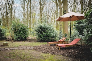 A garden with a wooden bench, a table with a red cushion, and a large umbrella. - Boshuisje Rekem - Arden (Lanaken)