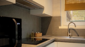 Een moderne keuken met een ingebouwde magnetron, een fornuis, een spoelbak en een raam met uitzicht op groen.