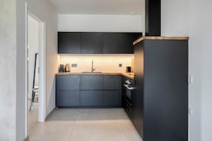 A modern kitchen with dark cabinetry, a stainless steel sink, and a built-in oven. - Hoeve de Eik, which sleeps eight, is a spacious and cosy apartment on the top floor, ideal for families or small groups. (Epen)