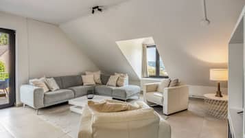 Un soggiorno moderno con un divano angolare grigio, una poltrona bianca e un divano beige. Si nota un tavolino da caffè, una lampada e vista all'esterno da una finestra.