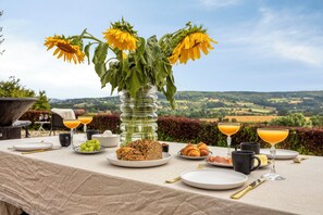 A table set for breakfast with a view of the countryside, including a glass vase with sunflowers, plates of food, and glasses of orange juice. - Hoeve de Eik, which sleeps eight, is a spacious and cosy apartment on the top floor, ideal for families or small groups. (Epen)