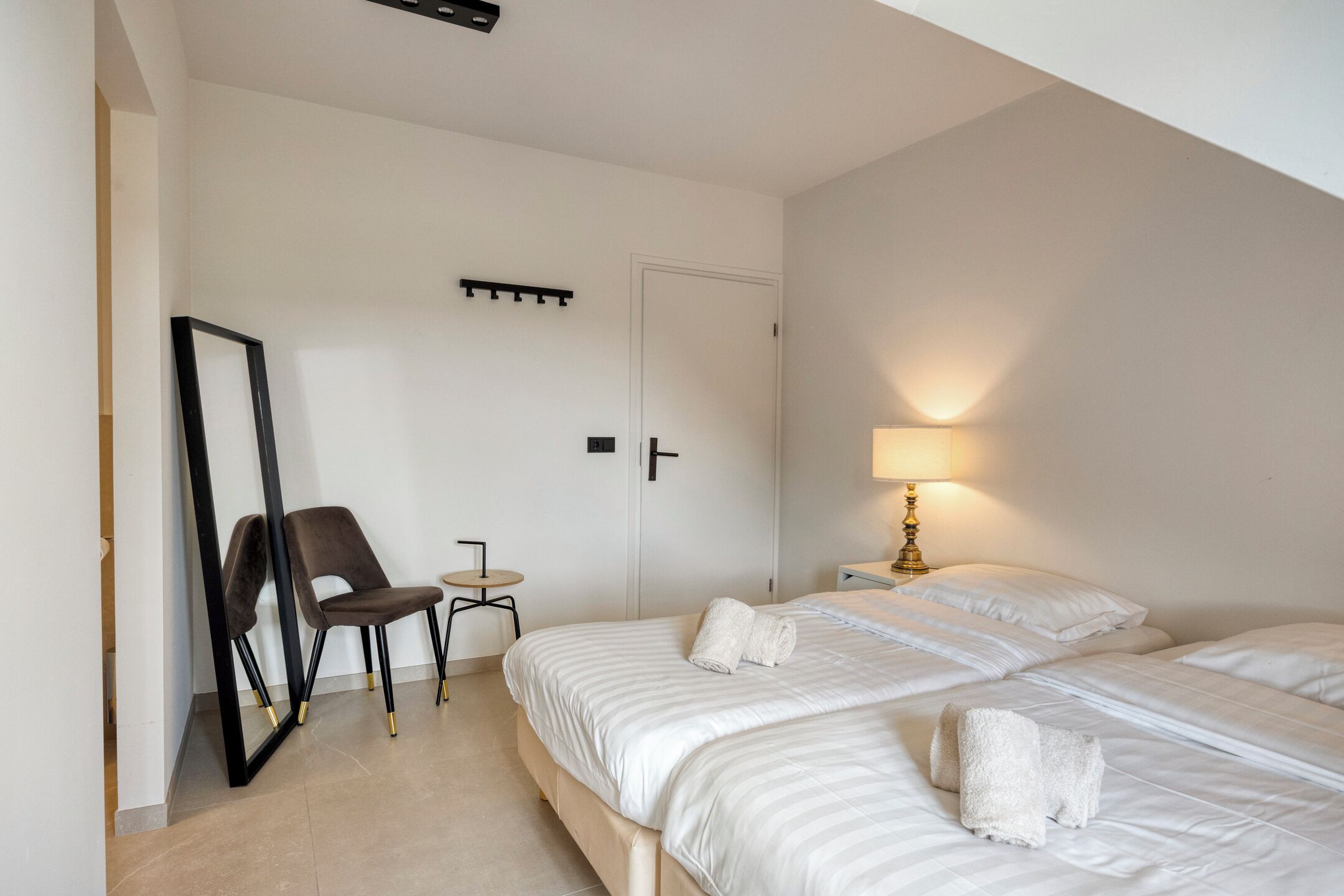 Een hotelkamer met twee bedden, een stoel, een tafeltje, een spiegel en een lamp.