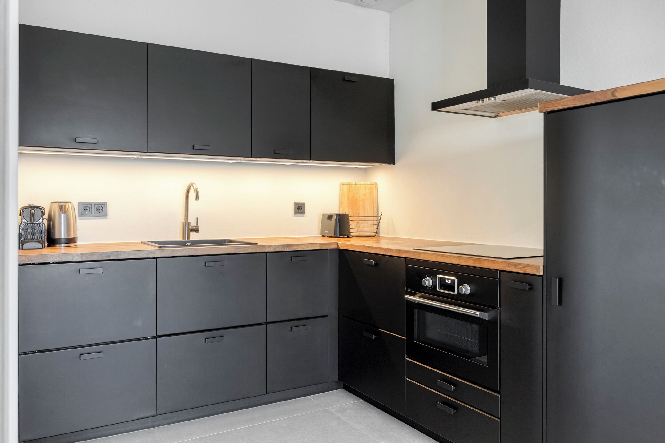 A modern kitchen with dark cabinetry, a stainless steel sink, a toaster, and a built-in oven.