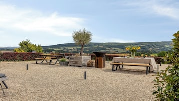 An outdoor seating area with tables and benches, surrounded by gravel, with a view of rolling hills in the background.