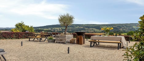 Un espace extérieur aménagé avec des tables et des bancs, entouré de gravier, et offrant une vue sur des collines verdoyantes en arrière-plan.