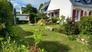 En bolighave med en sti, en stenbænk og mange forskellige planter og blomster.