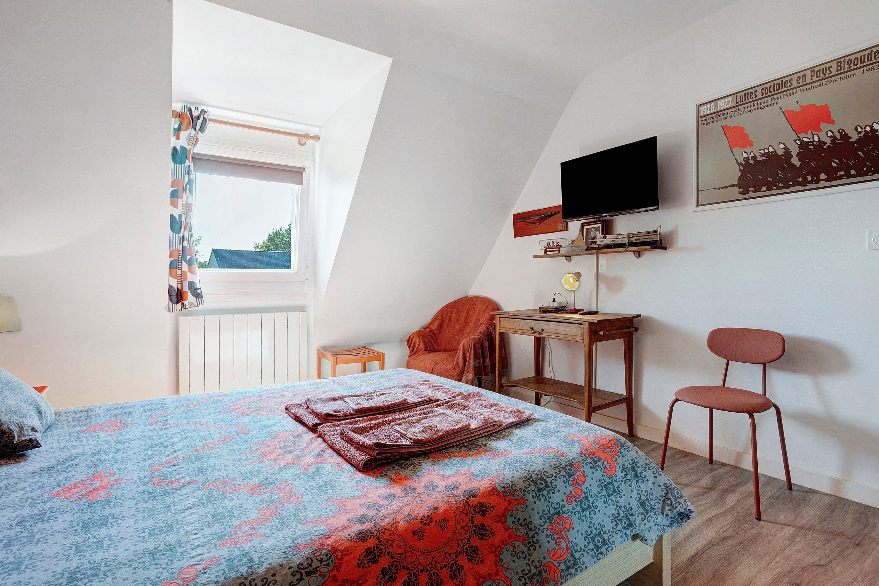 Ein Schlafzimmer mit einem Bett, einem Schreibtisch, einem Sessel, einem Fernseher und einem Fenster.