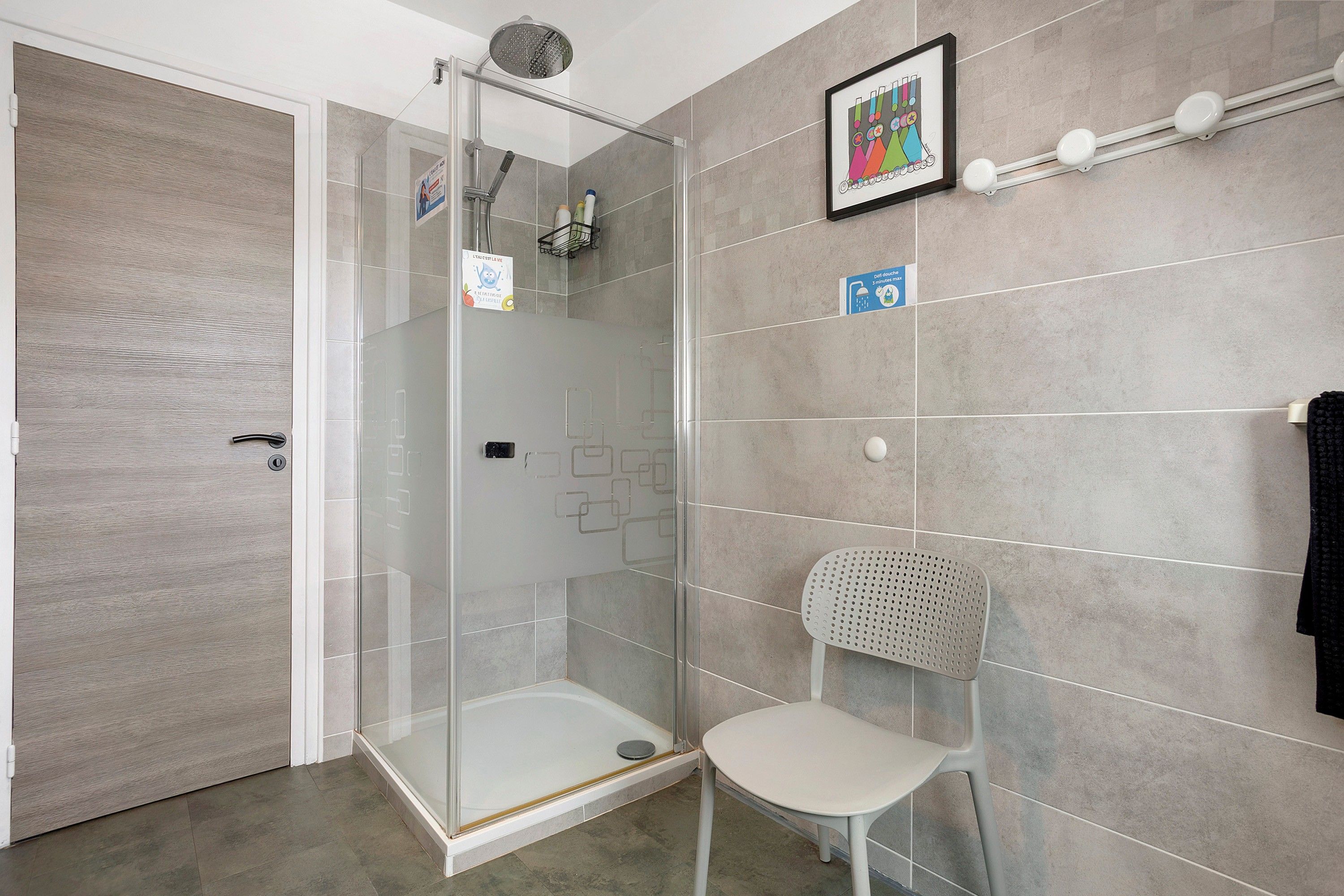 Une salle de bain moderne avec une douche à parois de verre, une chaise blanche et un porte-serviettes.