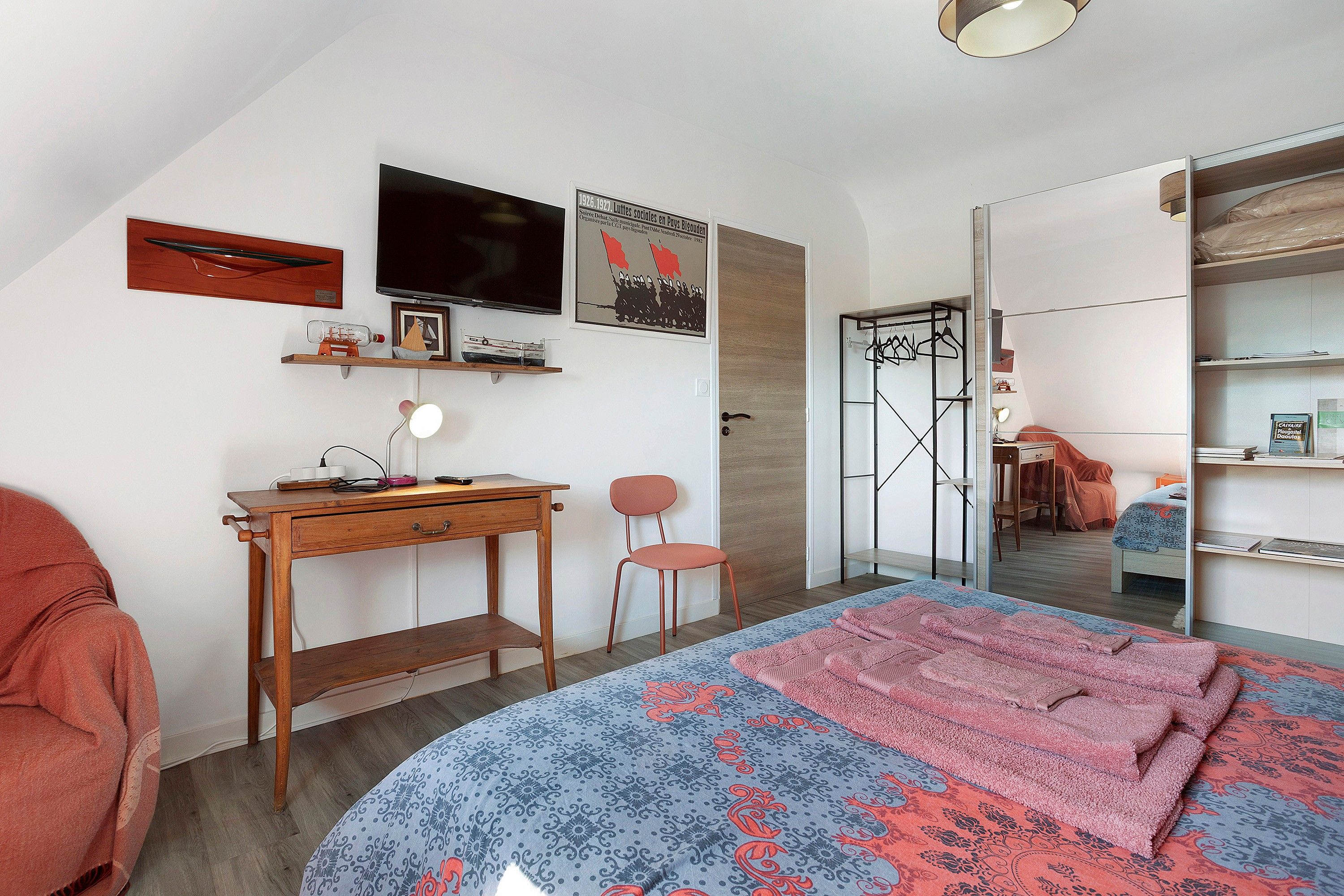 A bedroom with a bed, a desk, a chair, a wardrobe, and a mirror.