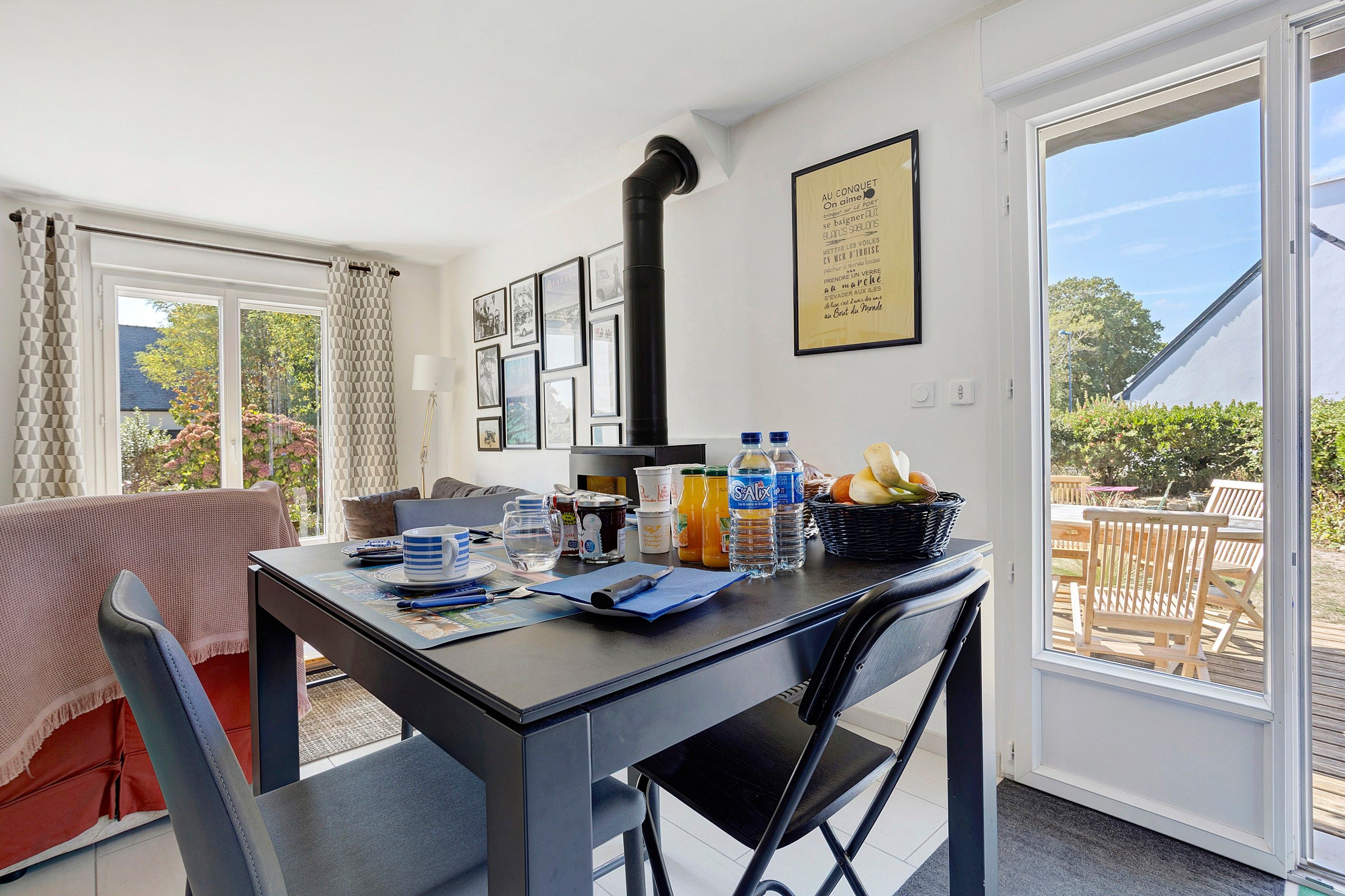 Un coin repas avec une table dressée pour deux personnes, une chaise noire, une fenêtre donnant sur l’extérieur et un mur orné de tableaux.