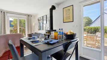 Un coin repas avec une table dressée pour deux personnes, une chaise noire, une fenêtre donnant sur l’extérieur et un mur orné de tableaux.