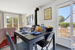 Un coin repas avec une table dressée pour deux personnes, une chaise noire, une fenêtre donnant sur l’extérieur et un mur orné de tableaux.