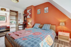 Une chambre avec un plafond en pente, un lit recouvert d’une literie à motifs, deux lampes de chevet et des œuvres d’art accrochées aux murs.