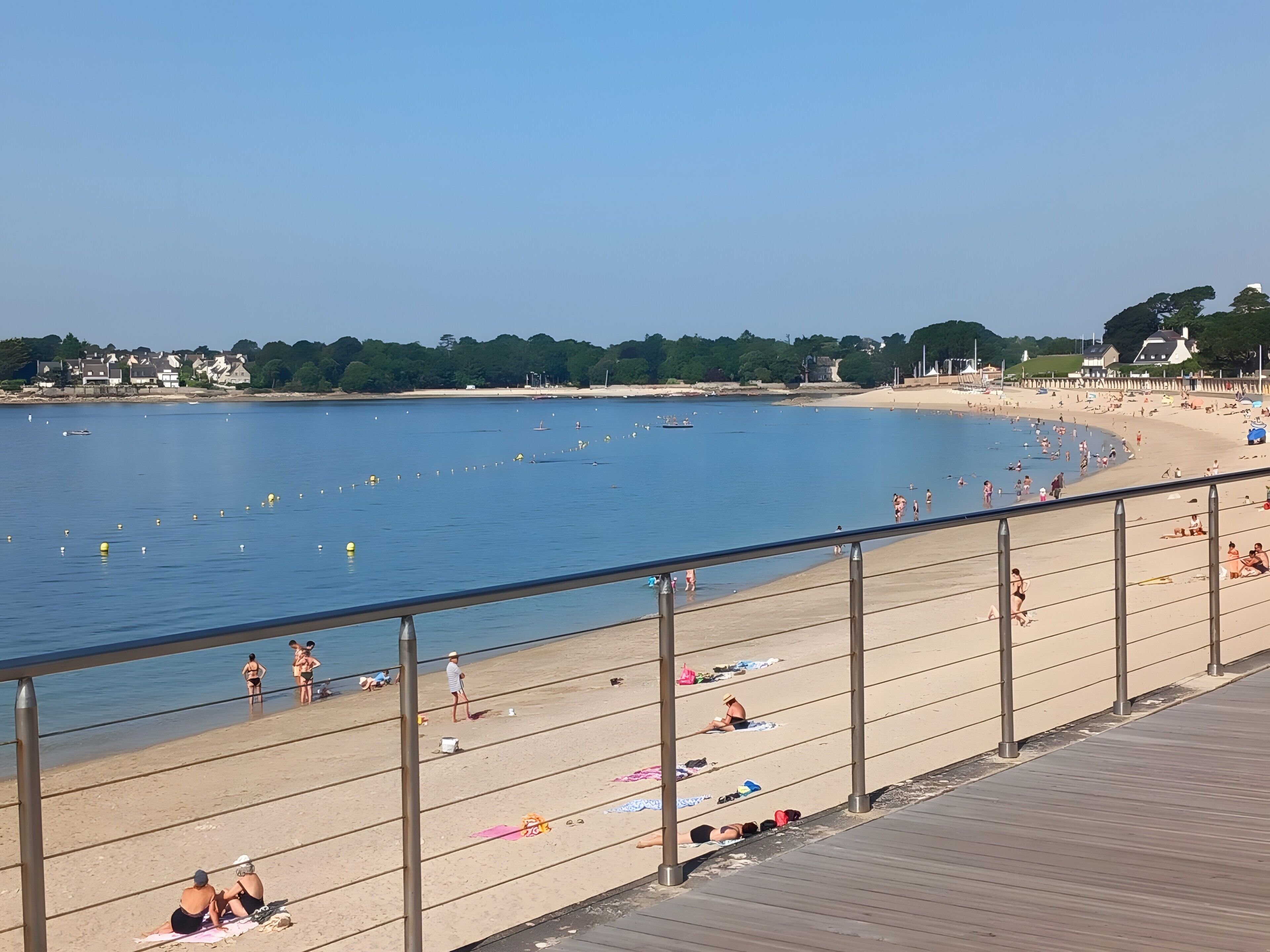 A beach with a wooden boardwalk, people sunbathing, and a clear blue sky.