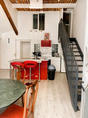 A modern kitchen with a red refrigerator, a dining area with a green table and red chairs, and a staircase with a black railing. - Former Loft Studio, 105 m² • Air Conditioning • Vaulted Cellar • The Heart of Aix's Historic Center (Aix-en-Provence)