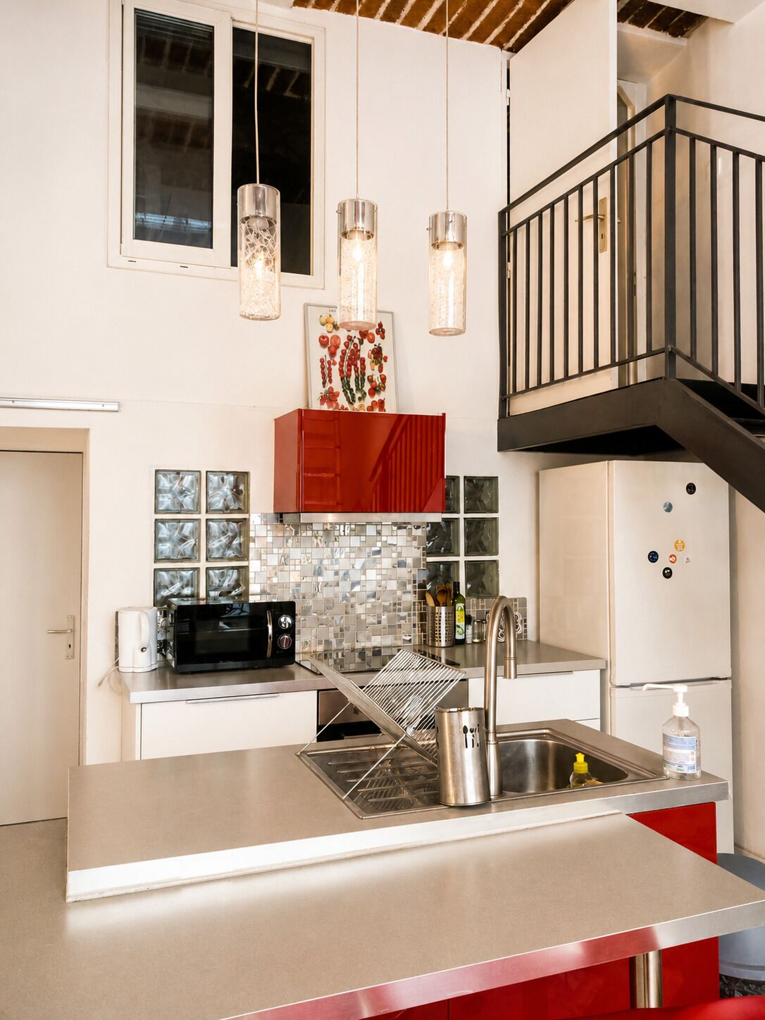 A modern kitchen with a stainless steel countertop, a built-in microwave, a sink, and a red cabinet.