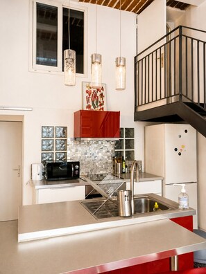 A modern kitchen with a stainless steel countertop, a built-in microwave, a sink, and a red cabinet. - Former Loft Studio, 105 m² • Air Conditioning • Vaulted Cellar • The Heart of Aix's Historic Center (Aix-en-Provence)