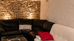 A living room with a stone wall, a black leather sofa, a white sofa, and a glass coffee table. - Former Loft Studio, 105 m² • Air Conditioning • Vaulted Cellar • The Heart of Aix's Historic Center (Aix-en-Provence)