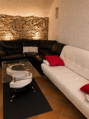 A living room with a stone wall, a black leather sofa, a white sofa, and a glass coffee table. - Former Loft Studio, 105 m² • Air Conditioning • Vaulted Cellar • The Heart of Aix's Historic Center (Aix-en-Provence)