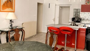 A dining area with a round table and chairs, a kitchen with red bar stools, and a painting on the wall. - Former Loft Studio, 105 m² • Air Conditioning • Vaulted Cellar • The Heart of Aix's Historic Center (Aix-en-Provence)