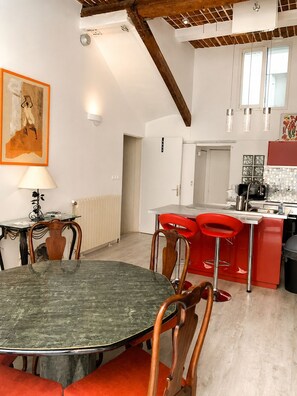 A dining area with a round table and chairs, a kitchen with red bar stools, and a painting on the wall. - Former Loft Studio, 105 m² • Air Conditioning • Vaulted Cellar • The Heart of Aix's Historic Center (Aix-en-Provence)
