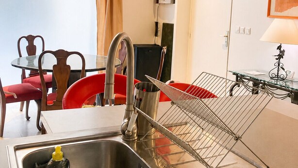 A modern kitchen with a stainless steel sink, a drying rack, and a dining area with red chairs. - Former Loft Studio, 105 m² • Air Conditioning • Vaulted Cellar • The Heart of Aix's Historic Center (Aix-en-Provence)