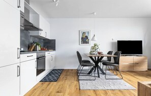 Eine moderne Küche mit weißen Schränken, einem Essbereich mit Tisch und Stühlen sowie einem Flachbildfernseher an der Wand.