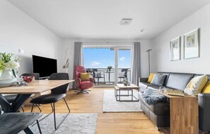 A modern living room with a dining area, a sofa set, and a view of the outdoors. - Biarritz - 2nd Floor, Balcony, Harbor View, Washing Machine, Private Parking (Olpenitz)