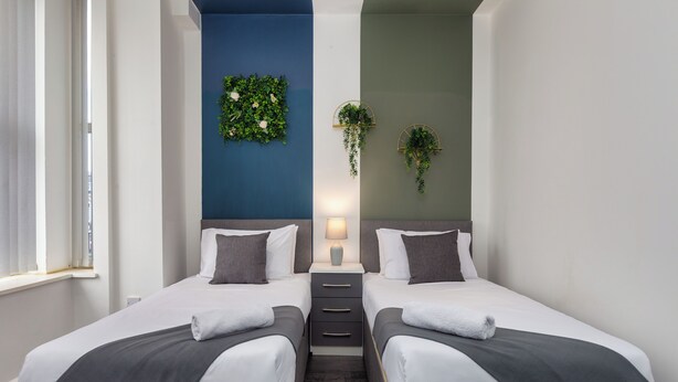 Una moderna camera d'hotel con due letti, una parete decorata in blu e piante verdi.
