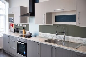 A modern kitchen with grey cabinets, a stainless steel sink, and a microwave. - South Pier Apartment 4 (Blackpool)