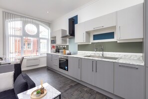 A modern kitchen with grey cabinets, a built-in oven, and a large window. - South Pier Apartment 4 (Blackpool)