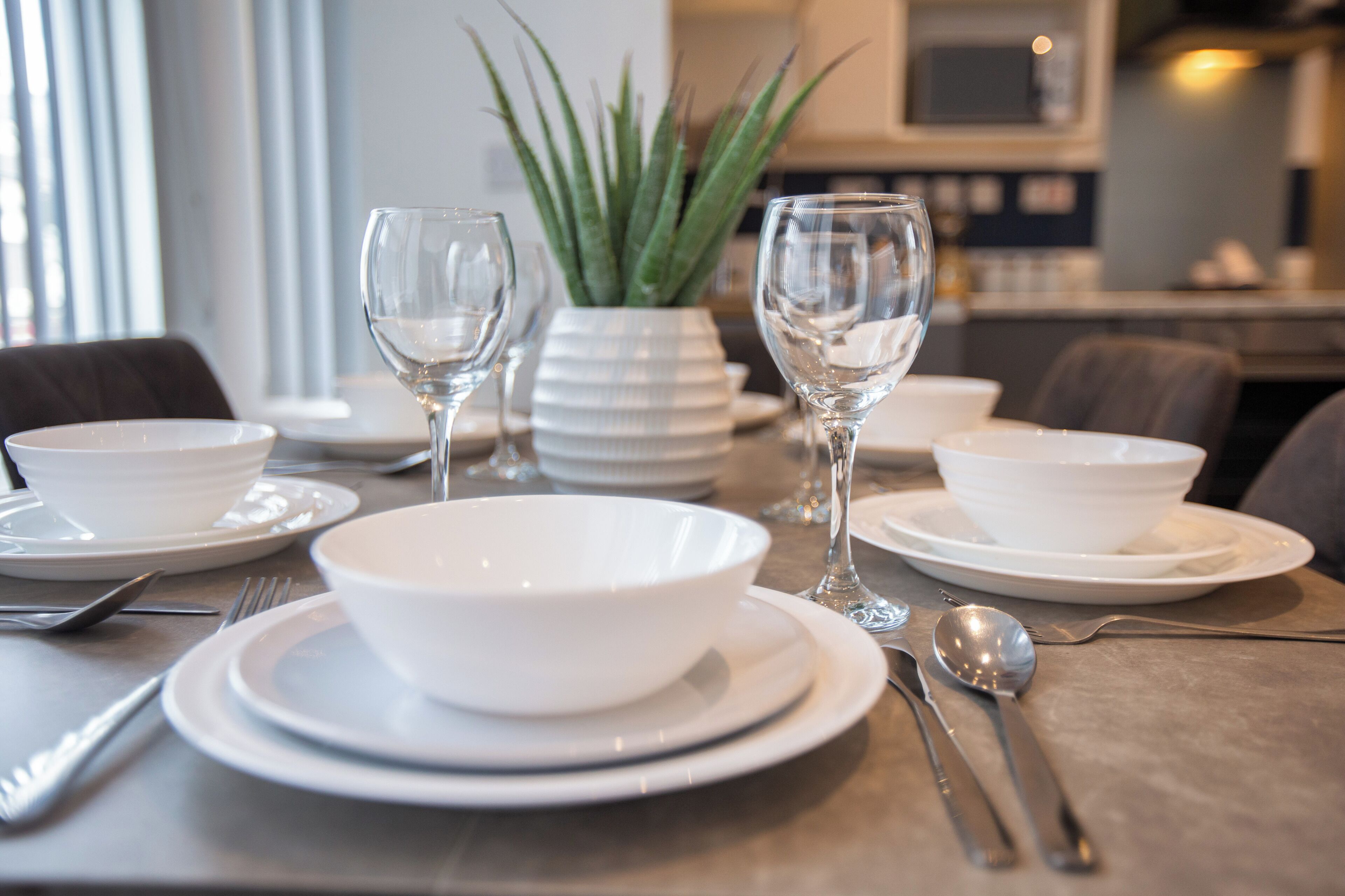 A dining table set with white plates, bowls, cutlery, and two wine glasses.