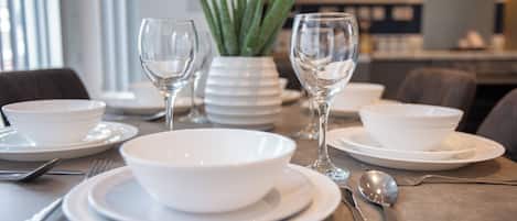 A dining table set with white plates, bowls, cutlery, and two wine glasses.