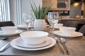 A dining table set with white plates, bowls, cutlery, and two wine glasses. - South Pier Apartment 3 (Blackpool)