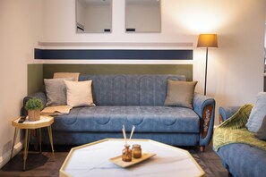 Ein modernes Wohnzimmer mit einer Couch, einem kleinen Beistelltisch, einer Stehlampe und einer dekorativen Tablett mit Kerzen.