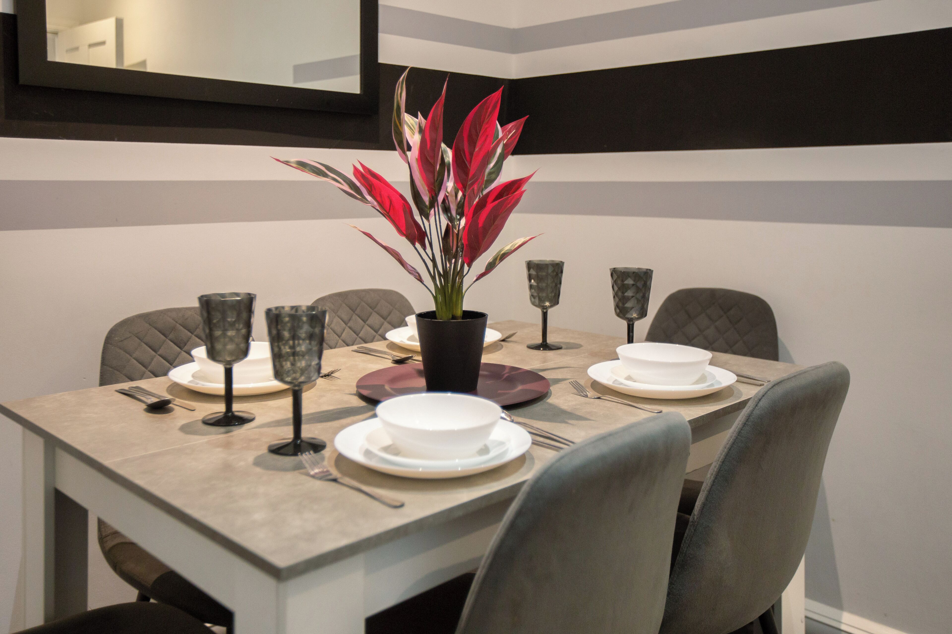 A dining table set with plates, glasses, and cutlery, with a potted plant in the center.